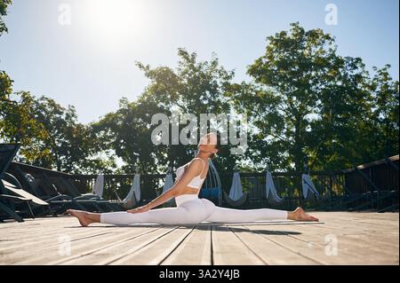 Practicing yoga exercises. Young woman in fitness clothes is outdoors. Stock Photo