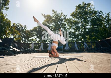 Practicing yoga exercises. Young woman in fitness clothes is outdoors. Stock Photo