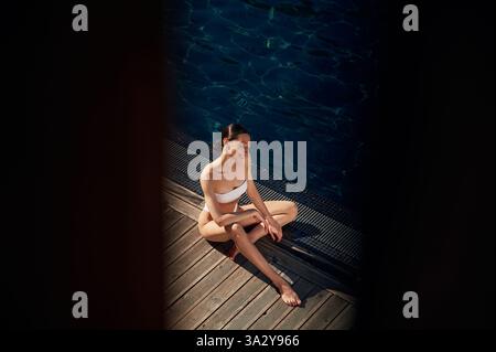 Resting, enjoying the vacation. Woman in white bikini is near swimming pool. Stock Photo