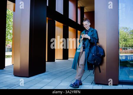 Student ginger girl near modern university building using a smartphone Stock Photo