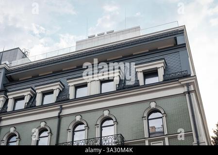 Upper floor of an old building with green tiled facade and beige window surrounds. Green house in old town with slate grey rooftop. Stock Photo