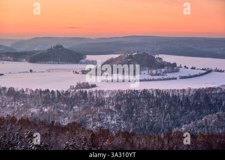Snow-covered winter landscape in the Saxon Switzerland National Park, the rock formations Zirkelstein and Kaiserkrone in the distance, at sunrise. Stock Photo