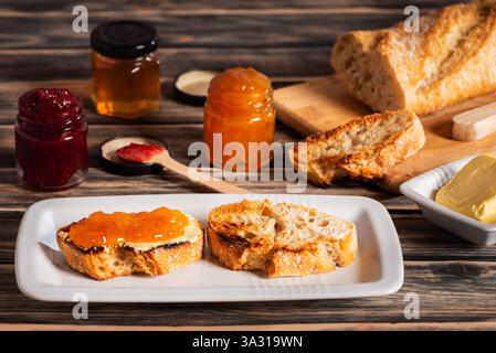 Preparations for making toast with butter and peach and raspberry jam, along with all their ingredients. Stock Photo