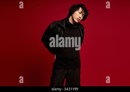 Stylish young Asian man in black poses against a red background. Stock Photo