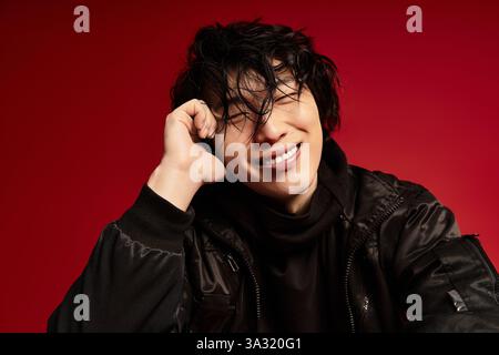 A young asian man strikes a fashionable pose in a red studio setting. Stock Photo