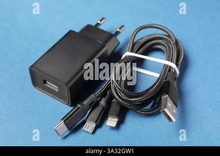 USB power adapter and triple charge cable on light blue background, closeup Stock Photo