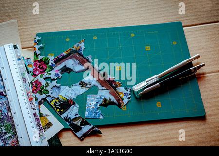 Crafting tools and materials on a green cutting mat, including a metal ruler, precision knives, and colorful paper cutouts, showcasing the creative pr Stock Photo