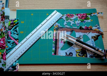 Crafting tools and materials on a green cutting mat, including a metal ruler, precision knives, and colorful paper cutouts, showcasing the creative pr Stock Photo