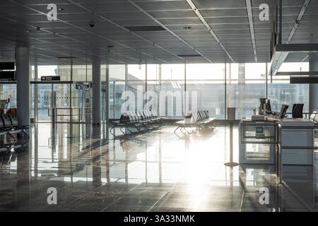 Empty rows of seats and benches inside international airport terminal. Departure waiting room near gate. Large windows, natural light, no people. Stock Photo