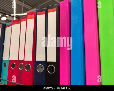 Brightly colored binders are arranged neatly on shelves in a bustling office supply store. Each binder features a blank label for easy identification, Stock Photo