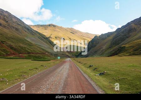 A captivating view of a dirt road winding through the vibrant, green and golden mountain valleys of Peru, showcasing the natural beauty and serene exp Stock Photo
