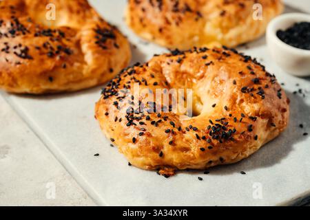 A close-up of golden brown bagels topped with black sesame seeds, resting on a white marble slab. Perfect for breakfast scenes, bakery promotions, and Stock Photo