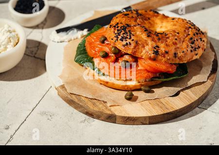 A gourmet bagel topped with smoked salmon, capers, and fresh greens on a wooden platter. The sesame seeds add texture, creating a mouthwatering, savor Stock Photo