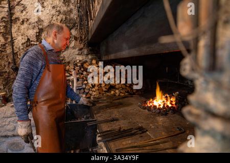 An elderly blacksmith works diligently in his Salzburg workshop, skillfully preserving centuries-old traditions of blacksmithing in the heart of Austr Stock Photo