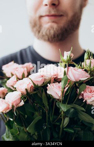 A bearded young man is holding a bouquet of pink roses. The focus is on the delicate, blooming roses while the background is softly blurred, creating Stock Photo