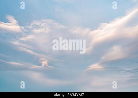 A serene sky captured at sunrise with wispy, flowing white clouds against a soft blue background. The scene conveys calmness, offering a peaceful and Stock Photo