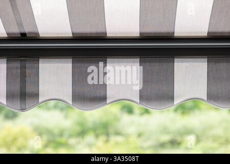 A close up view of a striped awning, showcasing its elegant wavy edge. The background is a garden green blur, highlighting the awning modern design an Stock Photo