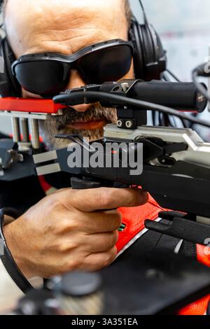 An experienced blind Olympic shooter aims with precision using advanced equipment. Wearing headphones and protective eyewear, they exemplify skill and Stock Photo