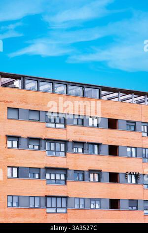 A striking photo showcasing an urban apartment facade with numerous windows and orange bricks, set against a clear blue sky. This vivid modern buildin Stock Photo