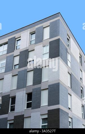 A clear shot of a modern urban building facade featuring a combination of textured wall panels in slate gray and white tones under a blue sky. Stock Photo