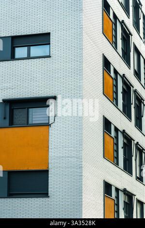 A detailed view of a modern urban building facade, featuring a stark contrast between white brick walls and vibrant orange panels around windows. Stock Photo