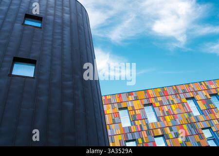 Low angle of a striking architectural contrast between a sleek, dark, curved facade and a vibrant multicolored building, showcasing a blend of modern Stock Photo