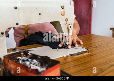 A asian seamstress works on a sewing machine in a studio, delicately stitching fabric. The close up view captures skilled hands, emphasizing craftsman Stock Photo
