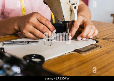 Hands of a asian seamstress using a vintage sewing machine to stitch fabric. The wooden table holds scissors and threads, illustrating traditional cra Stock Photo