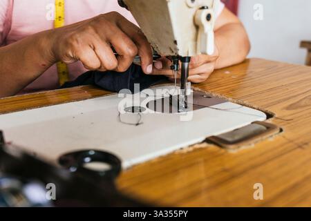 A detailed view of a asian seamstress hands operating a sewing machine. The fabric is being guided through the needle, showcasing precision and crafts Stock Photo