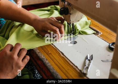 Close up of asian seamstress hands expertly sewing green fabric on a vintage sewing machine. The image captures the essence of traditional craftsmansh Stock Photo
