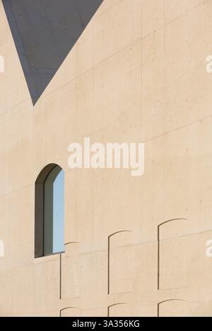 A minimalist hospital detail featuring beige concrete walls and arched window. Shadows create geometric patterns against the surface, enhancing the de Stock Photo