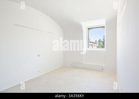 A bright, minimalist empty room of hospital with a single window. Natural light floods the space, highlighting the clean white walls and neutral floor Stock Photo