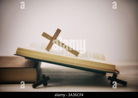 Old open Bible on a wooden table with several wooden crosses and isolated white background. Side view. Stock Photo
