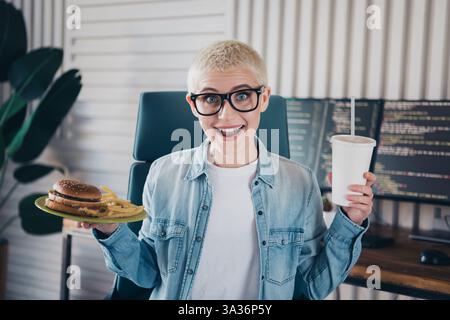 Young woman programmer enjoying a meal in a stylish workspace Stock Photo