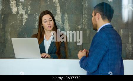 Professional interaction between businesswoman and businessman at reception, discussing project details with engaged expressions. Stock Photo