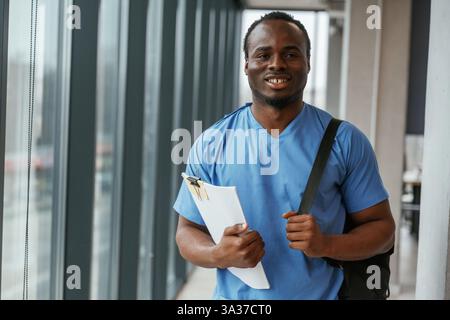 Black man doctor is standing indoors and holding documents in hands. Stock Photo