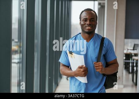Black man doctor is standing indoors and holding documents in hands. Stock Photo