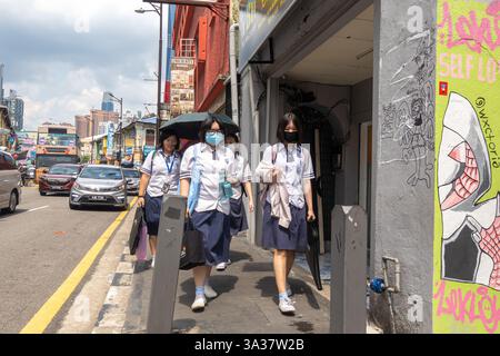 group of female students in school uniforms and face masks walking on a street, with umbrellas under heat, Kuala Lumpur Malaysia Stock Photo