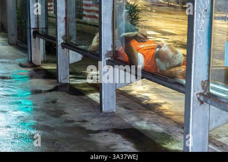 a homeless person lying sleeping on a bench a public bus station in the night,  Kuala Lumpur, Malaysia Stock Photo