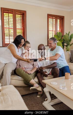 Senior Friends enjoying time together, laughing and sharing moments on smartphone at home Stock Photo