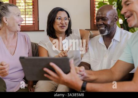Diverse senior group enjoying conversation while using digital tablet at home Stock Photo