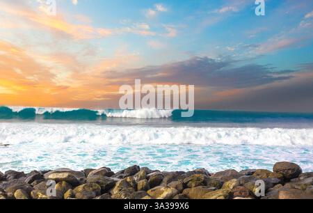 Powerful ocean wave breaking at sunset with colorful sky over rocks Stock Photo