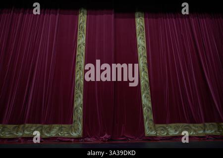 A close-up of a red curtain with vertical pleats, illuminated in a theatrical setting, showing the rich dense texture of the fabric with room to copy. High quality photo Stock Photo