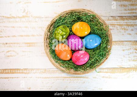 Small basket with colorful Easter eggs on a white painted wooden background, high angle view from above, copy space, selected focus, narrow depth of f Stock Photo