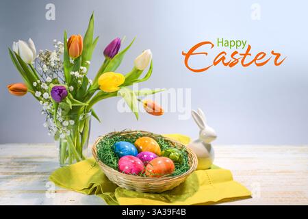 Colorful Easter eggs in a basket, spring bouquet with tulips and a small bunny, text Happy Easter, light blue gray background, copy space, selected fo Stock Photo