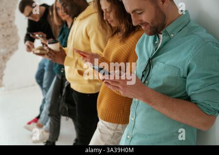 Side view. With smartphones in hands. Group of young people are standing against white background. Stock Photo