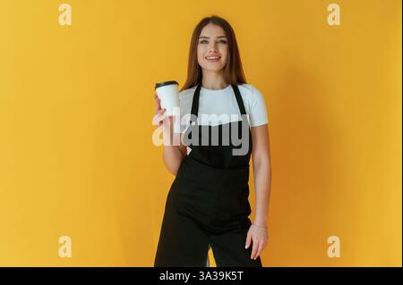 Nice coffee cup. Young woman is against yellow background. Stock Photo