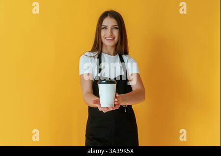 Nice coffee cup. Young woman is against yellow background. Stock Photo