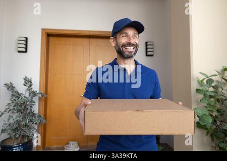 Happy Latin deliveryman in blue uniform carrying parcel Stock Photo