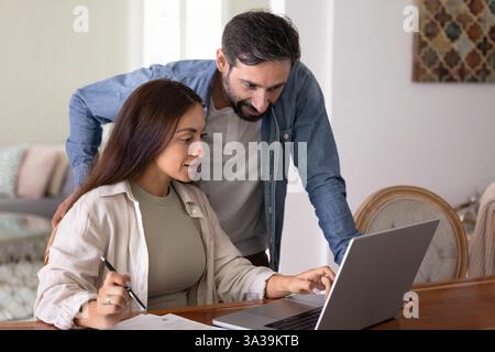 Positive husband and wife using online bank application on laptop Stock Photo